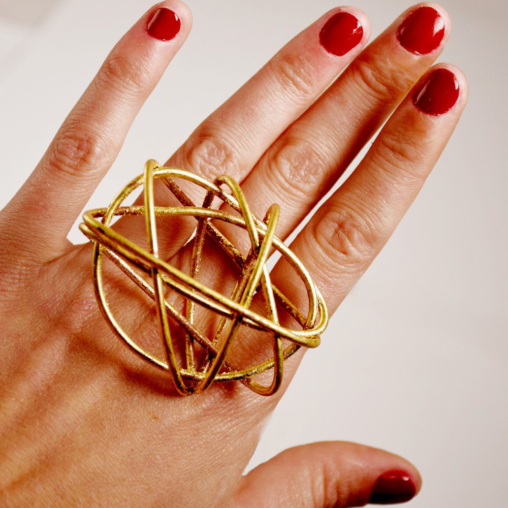 A hand wearing a large, abstract gold ring, with red-painted nails.