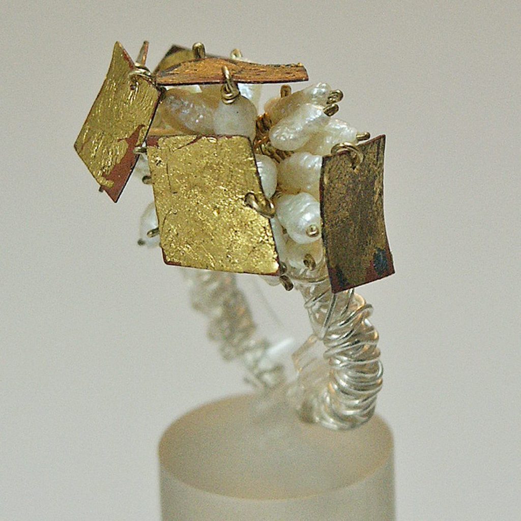 Bague artisanale ornée de perles blanches et de motifs dorés.