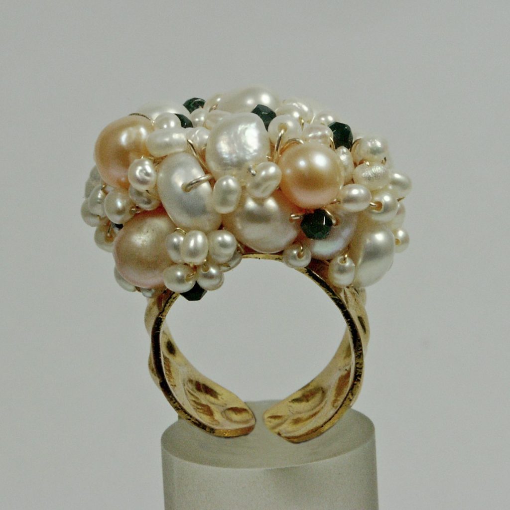 Artisan ring adorned with various pearls and gemstones, set on a display stand.