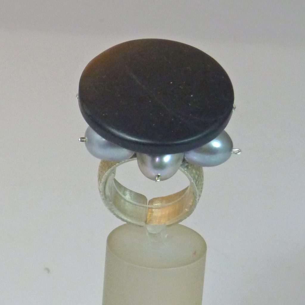 Bague en argent avec une pierre noire centrale et des perles grises sur les côtés.