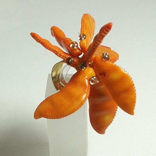 Bague ornée de pétales orange et de petites perles, sur un support doré, sur fond blanc.