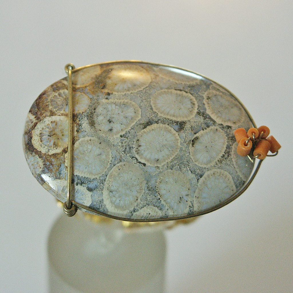 Bague en pierre polie avec motifs en spirale sur un fond beige, maintenue par un support en métal doré.