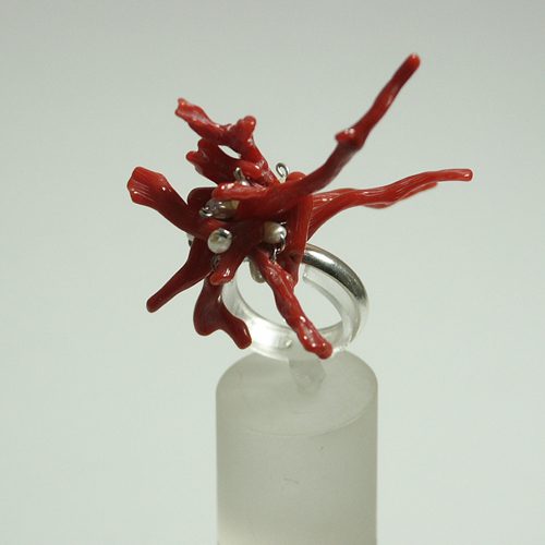 Bague en corail rouge avec des branches organiques sur un support transparent.