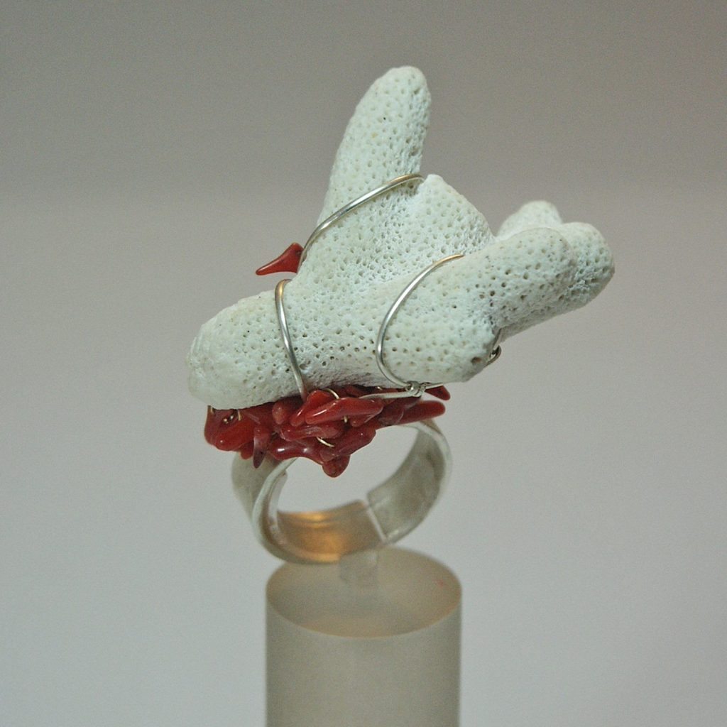 Bague artistique en corail rouge et pierre poreuse, présentée sur un support.