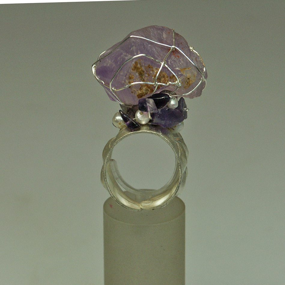 Bague artisanale avec une pierre améthyste entourée de fil métallique, ornée de cristaux et perles.