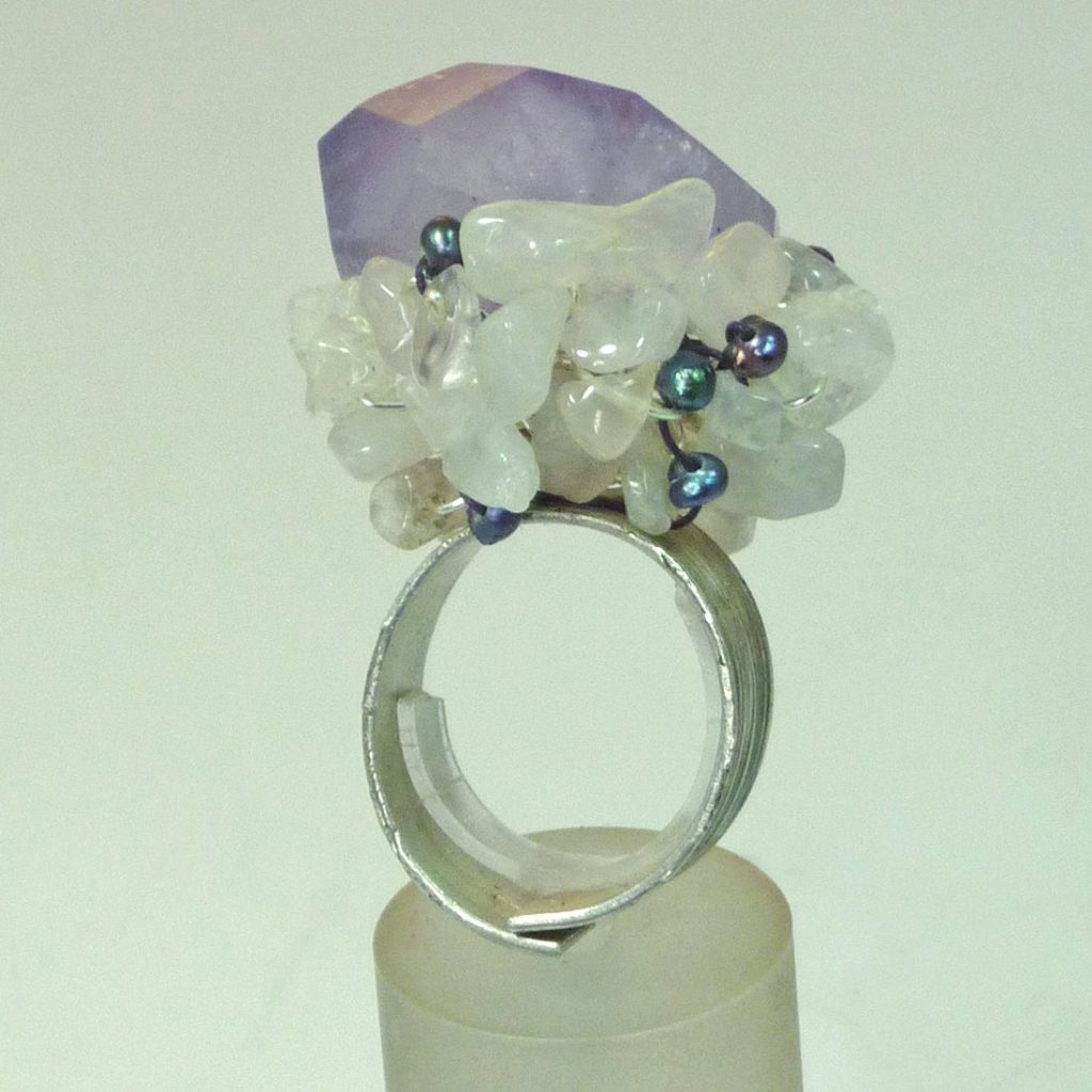 Bague en argent ornée d'une large pierre violet et de petites perles colorées, présentée sur un support.