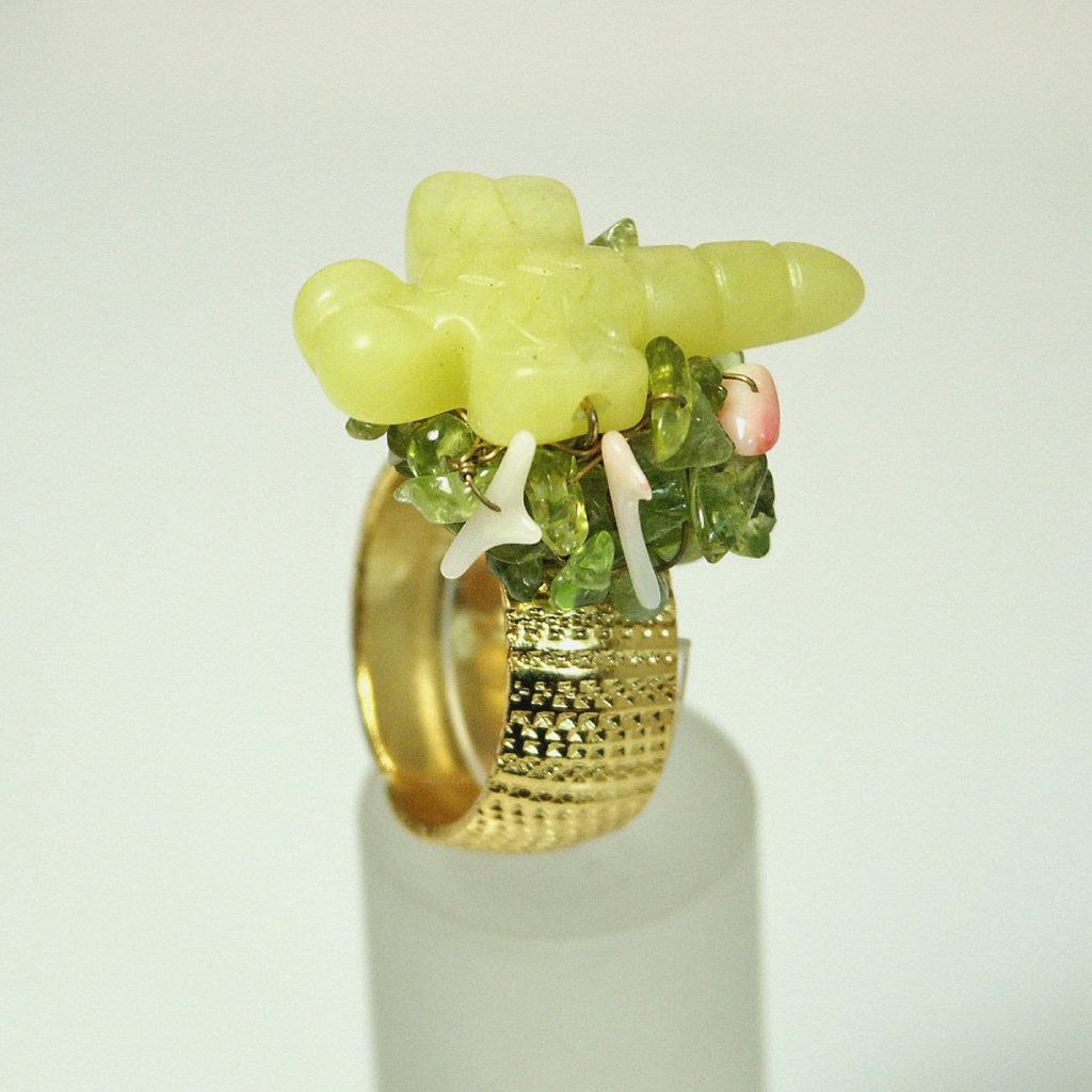 A unique gold ring featuring a carved yellow-green gemstone design on top, adorned with small green and pink decorative stones.
