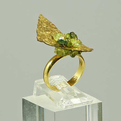 Bague en or ornée de perles vertes, présentée sur un support transparent.