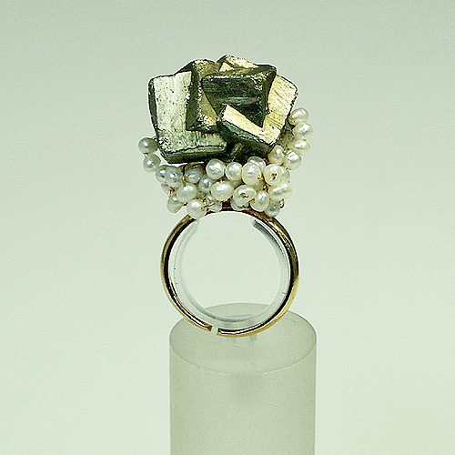 Bague en argent ornée d'un cristal de pyrite, entourée de perles blanches, sur un support transparent.