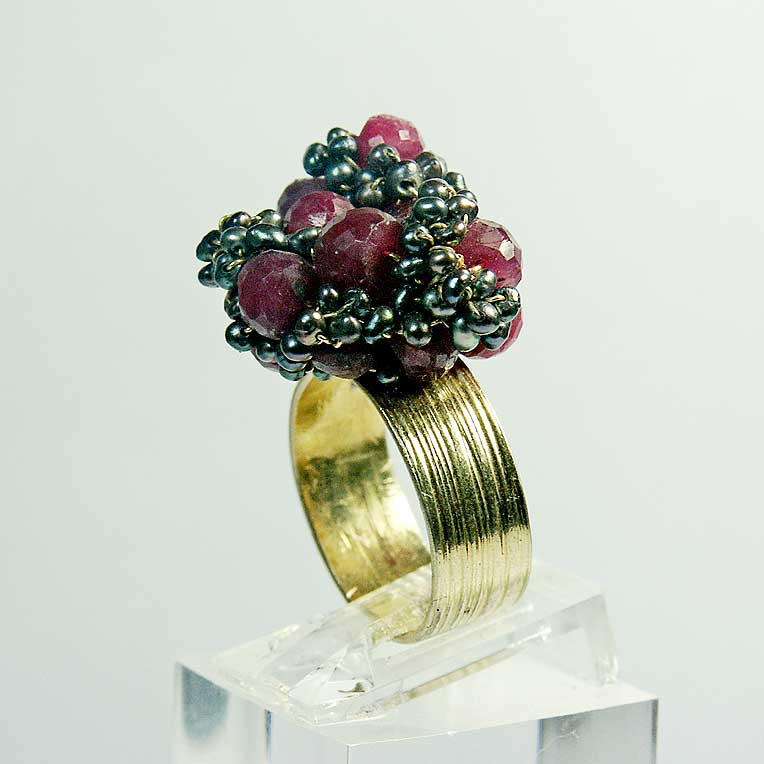 Bague ornée de pierres rouges et d'un design texturé en métal doré, présentée sur un support transparent.