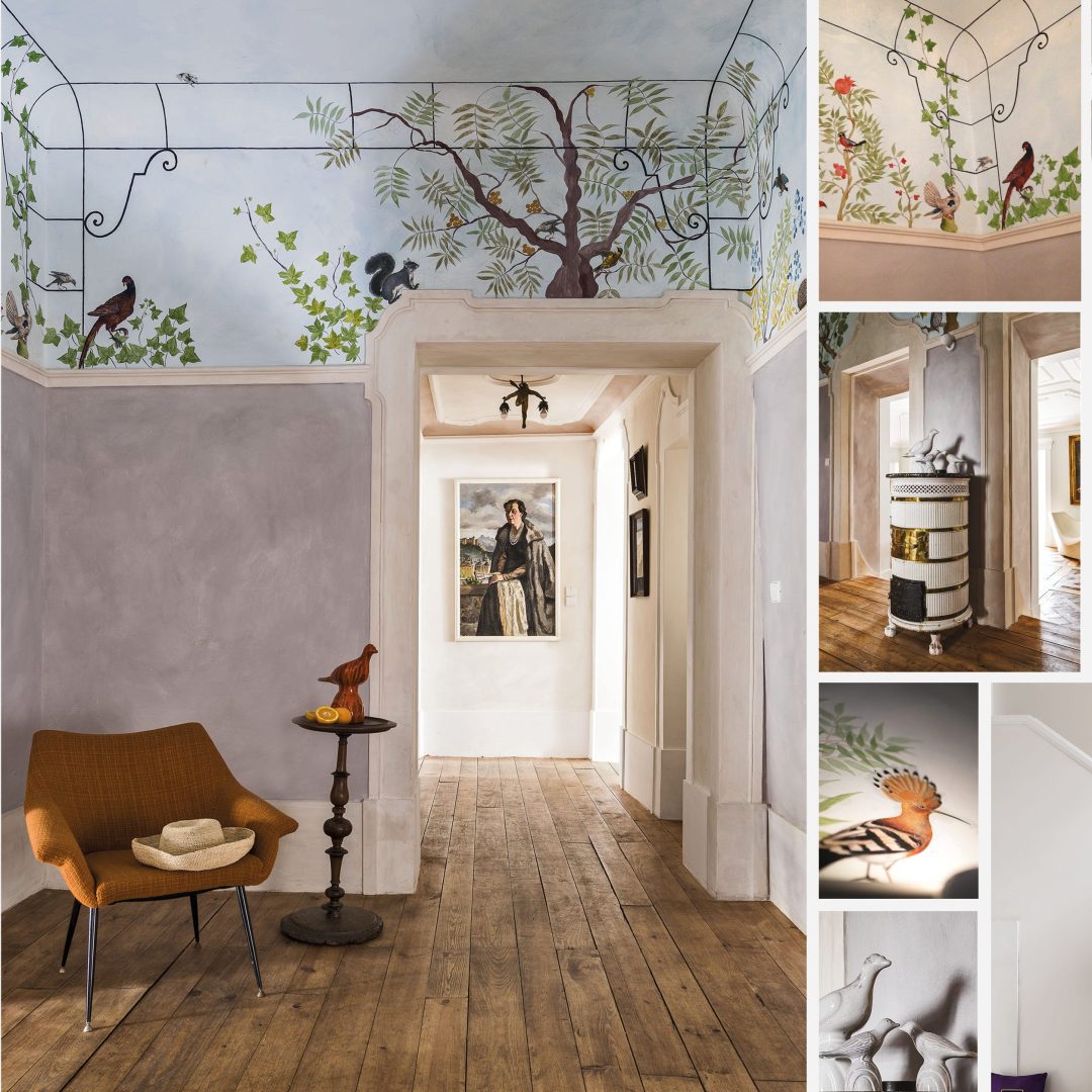 Intérieur de La Maison du Lynx avec un mur décoré de fresques représentant des arbres et des oiseaux, un fauteuil orange, une table avec une décoration et un tableau sur le mur opposé.