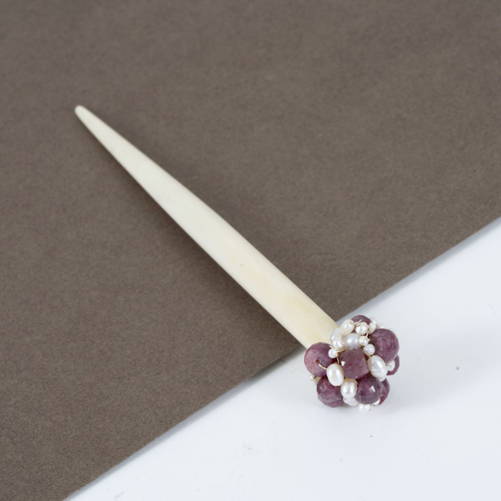 Peigne orné de perles et de pierres précieuses, posé sur un fond gris.