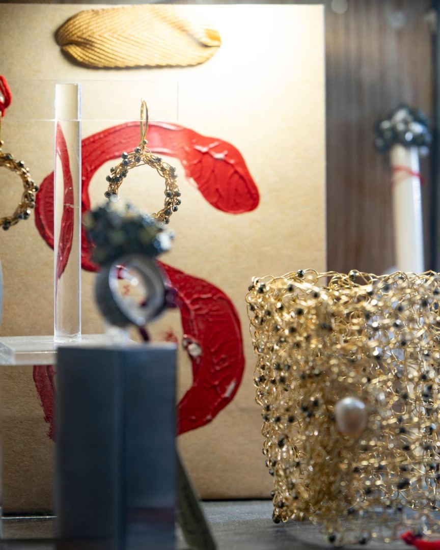 Bijoux en or affichés sur un fond de papier avec des motifs rouges, incluant des boucles d'oreilles et un bracelet décoré de perles.