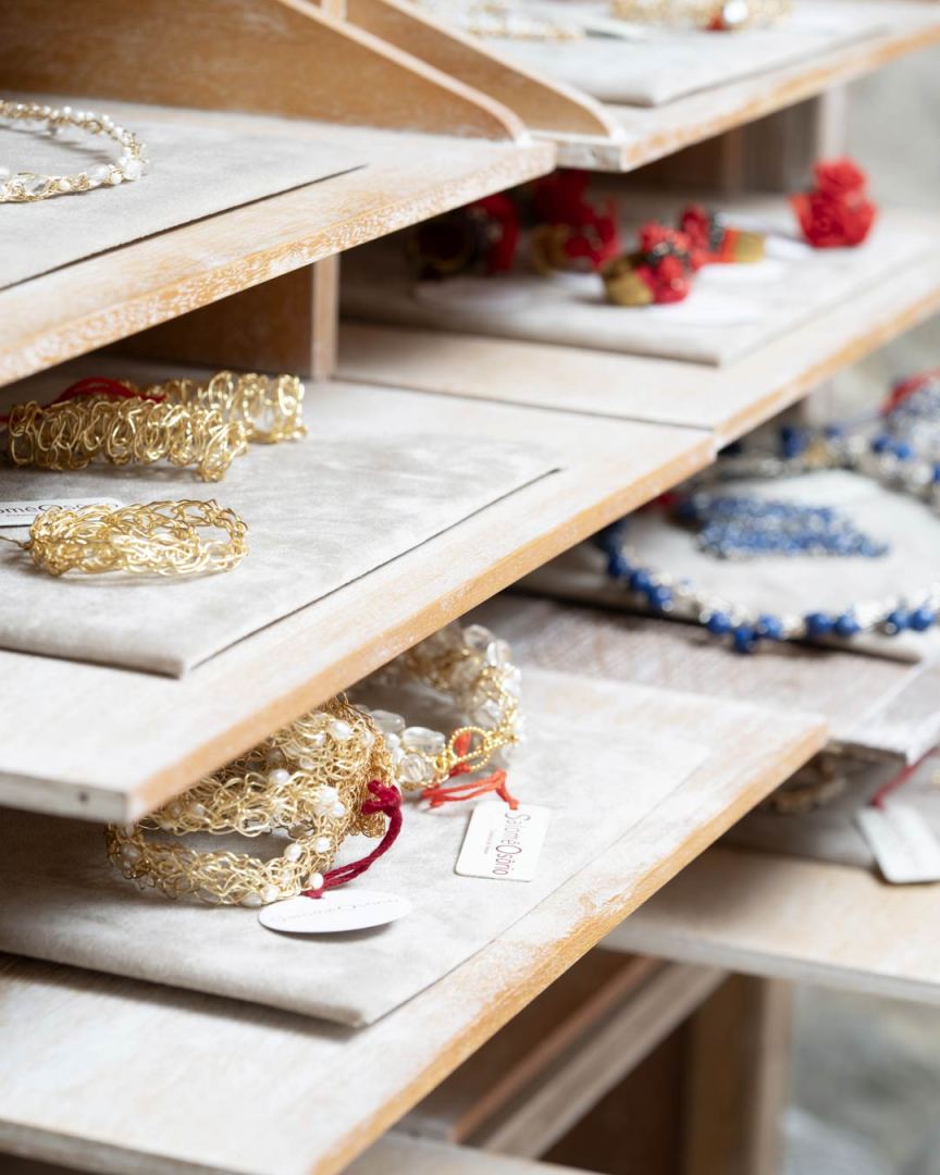 Rangement de bijoux sur des étagères en bois, comprenant des bracelets dorés et des colliers colorés.