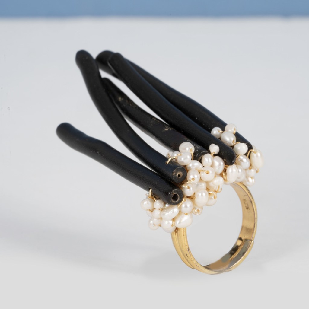 Bague unique avec plusieurs tiges noires et des perles blanches, sertie sur un anneau en or.