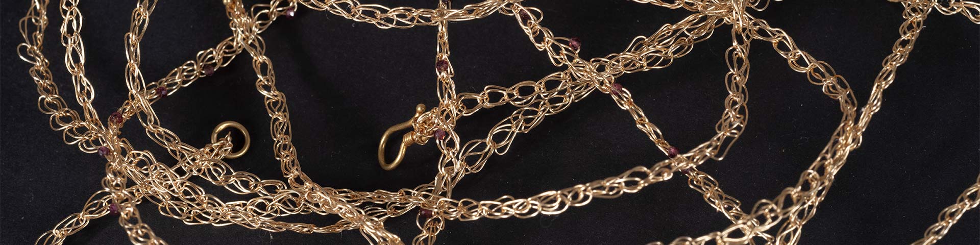 A close-up of intricate golden chains styled in a decorative arrangement on a dark background.